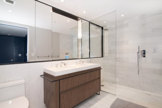 bathroom featuring tiled shower, vanity, toilet, and tile walls