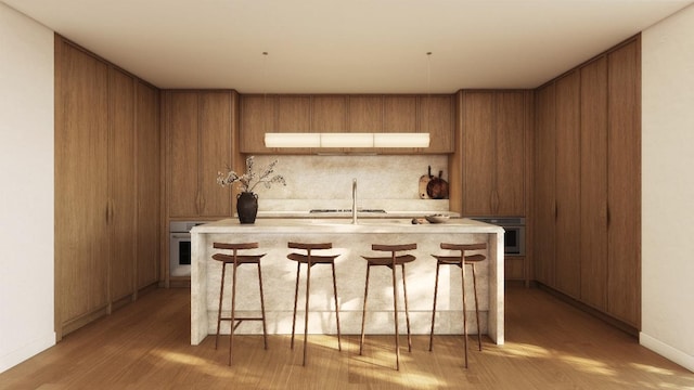 kitchen featuring sink, a breakfast bar area, black oven, and a center island with sink