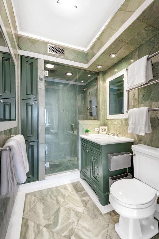 bathroom featuring a shower with door, tile walls, vanity, ornamental molding, and toilet