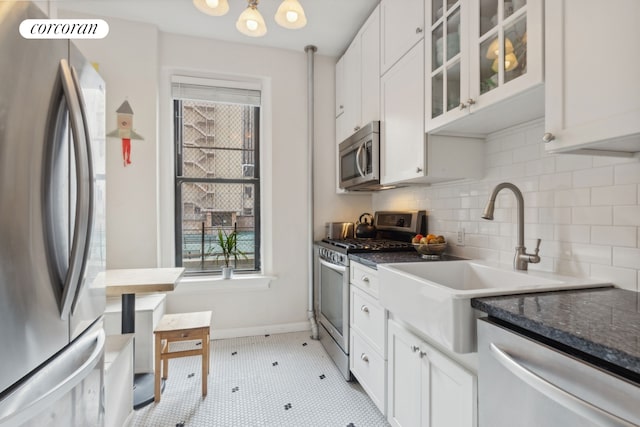 kitchen with a sink, backsplash, white cabinetry, appliances with stainless steel finishes, and glass insert cabinets