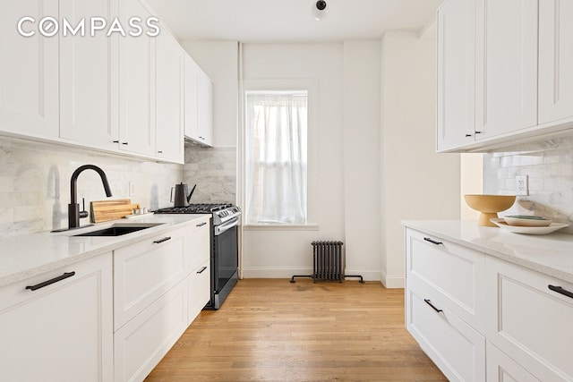 kitchen with light stone counters, stainless steel range with gas cooktop, a sink, white cabinets, and light wood-type flooring