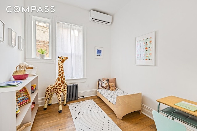 bedroom featuring a wall mounted air conditioner, baseboards, radiator, and light wood-style flooring