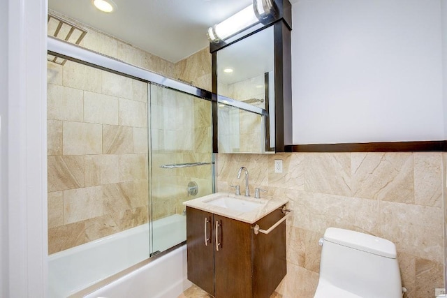 full bathroom with tile walls, vanity, combined bath / shower with glass door, and toilet