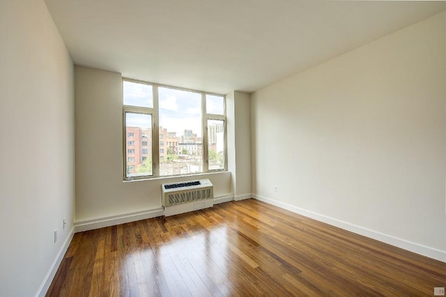 spare room with a view of city, an AC wall unit, wood finished floors, and baseboards