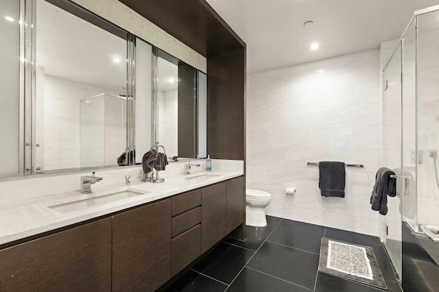 bathroom with a stall shower, tile patterned floors, toilet, double vanity, and tile walls