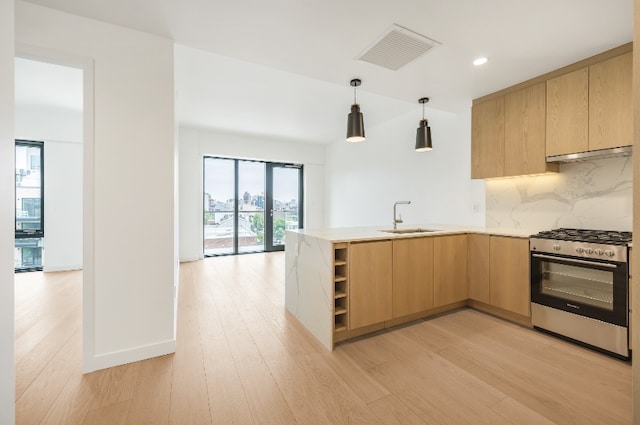 kitchen with sink, light brown cabinets, gas range, kitchen peninsula, and light wood-type flooring