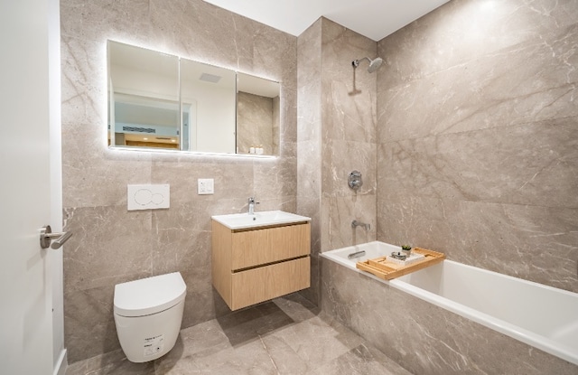 full bathroom featuring tiled shower / bath, vanity, toilet, and tile walls