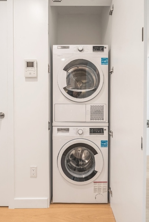 laundry room with stacked washer and dryer and light hardwood / wood-style flooring