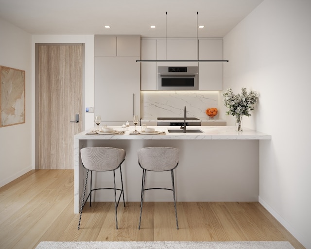 kitchen featuring sink, a breakfast bar area, backsplash, light hardwood / wood-style floors, and stainless steel oven