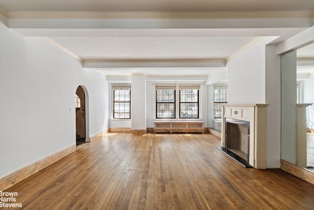 unfurnished living room featuring wood-type flooring, ornamental molding, and radiator