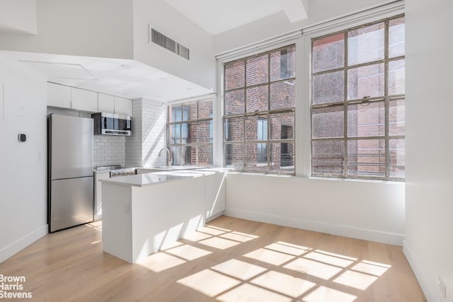 kitchen with stainless steel appliances, visible vents, white cabinets, light wood-type flooring, and tasteful backsplash