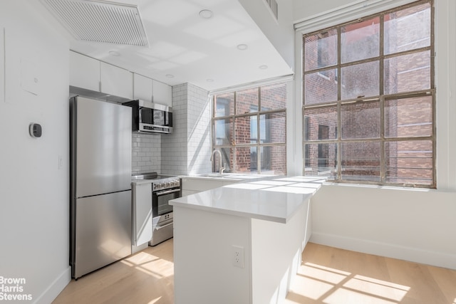 kitchen featuring a peninsula, light wood-style flooring, white cabinetry, and stainless steel appliances