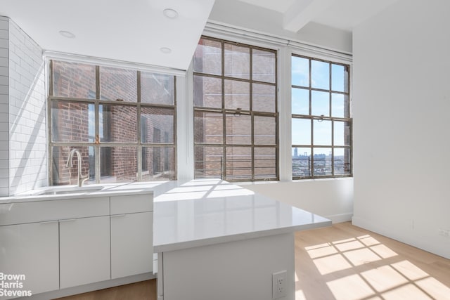 interior space with light wood-style flooring, baseboards, a sink, and beamed ceiling