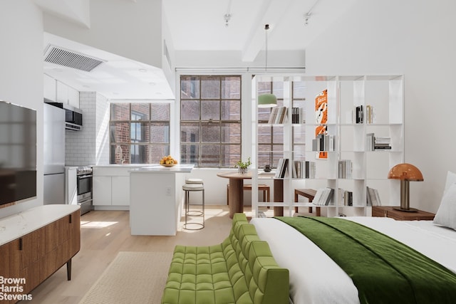 bedroom with beam ceiling, light hardwood / wood-style floors, and stainless steel refrigerator