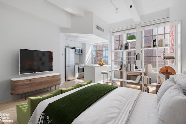 bedroom featuring stainless steel fridge, beamed ceiling, visible vents, and light wood finished floors