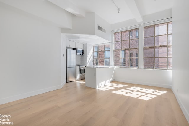 spare room featuring light wood-style floors, baseboards, visible vents, and beam ceiling