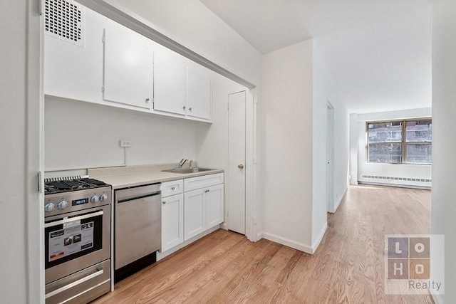 kitchen featuring visible vents, baseboard heating, appliances with stainless steel finishes, a sink, and light wood-type flooring