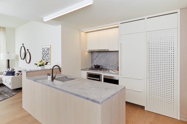 kitchen featuring oven, a sink, backsplash, light wood finished floors, and modern cabinets