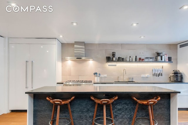 bar featuring sink, white cabinetry, tasteful backsplash, light hardwood / wood-style floors, and wall chimney exhaust hood