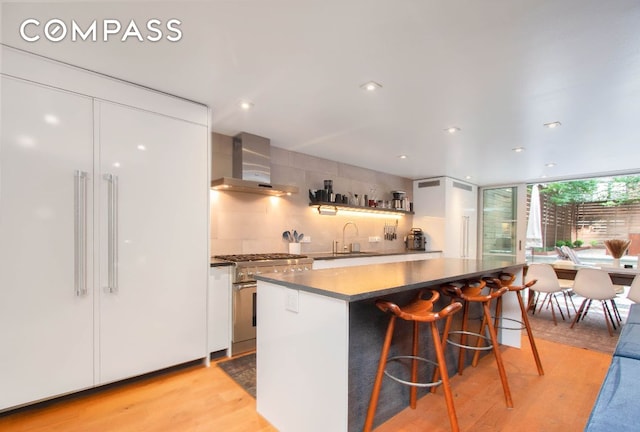 kitchen with wall chimney range hood, sink, light hardwood / wood-style flooring, high end range, and white cabinets