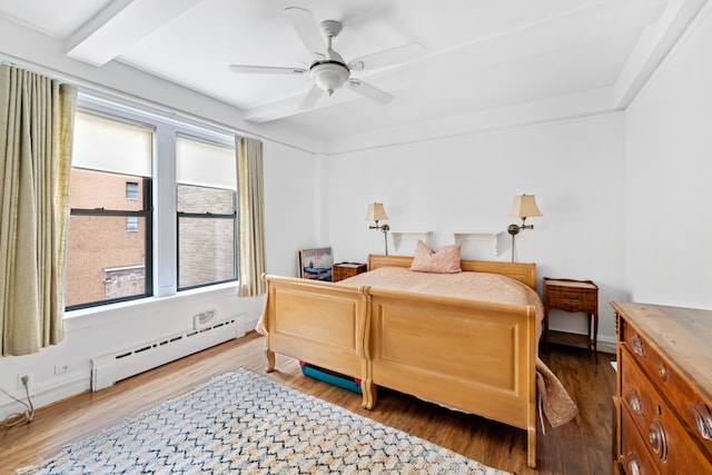 bedroom featuring a baseboard heating unit, multiple windows, and wood finished floors