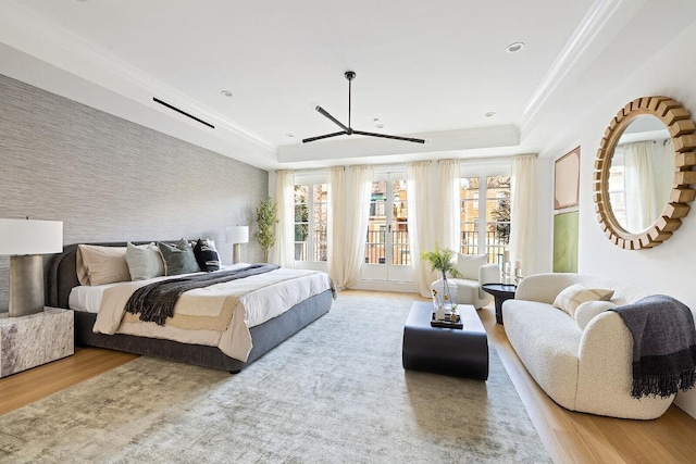 bedroom featuring access to exterior, a tray ceiling, crown molding, and light wood-type flooring