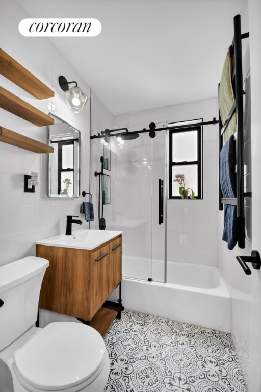 full bathroom with combined bath / shower with glass door, tile patterned flooring, tile walls, vanity, and toilet