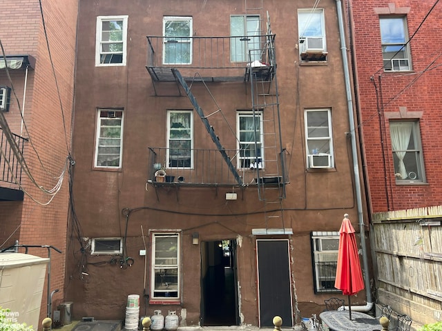 rear view of property with cooling unit, a balcony, and stucco siding