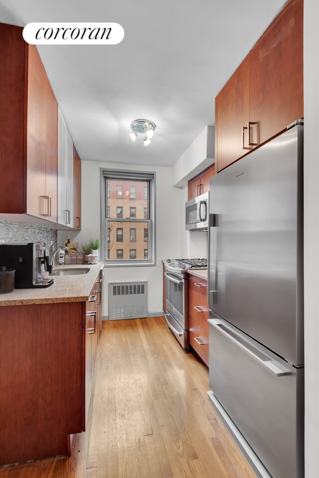 kitchen featuring sink, tasteful backsplash, light hardwood / wood-style flooring, radiator, and stainless steel appliances