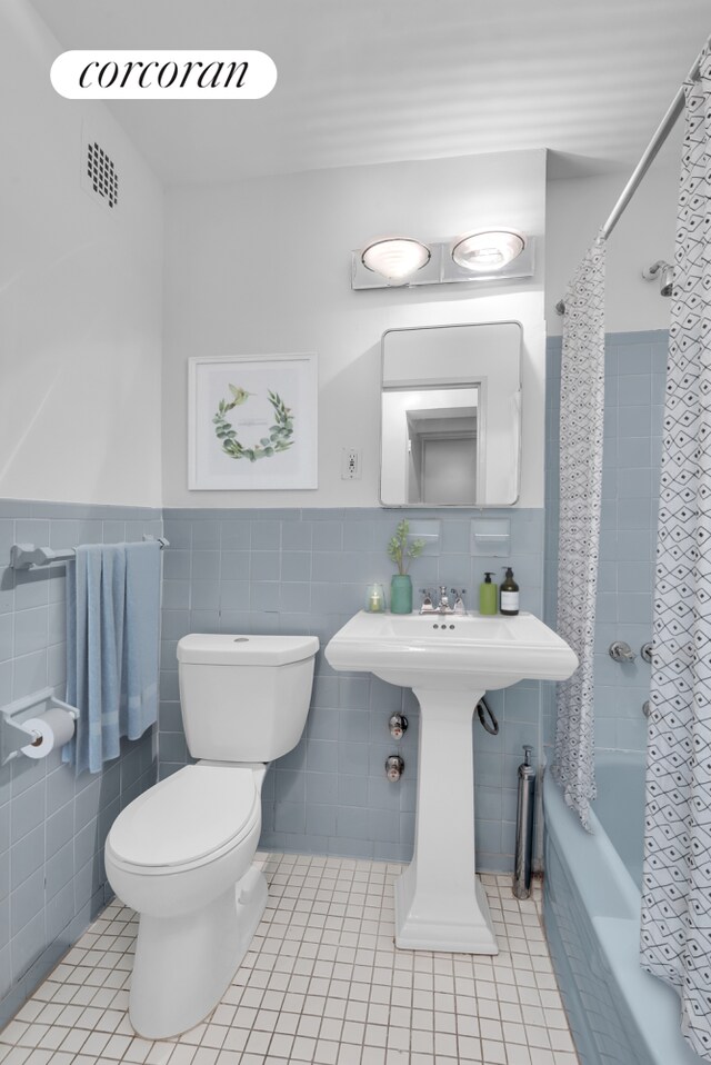 bathroom with tile patterned floors, toilet, shower / tub combo, and tile walls