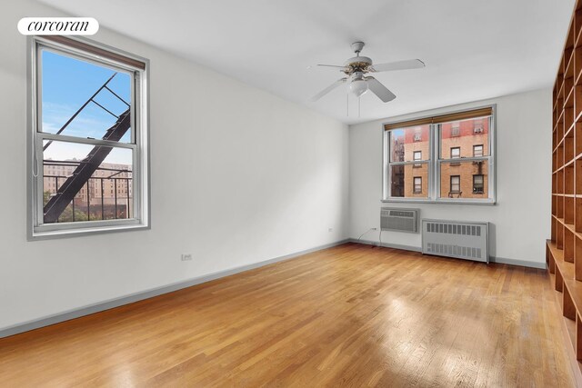 interior space featuring radiator, light hardwood / wood-style floors, a wall mounted AC, and ceiling fan