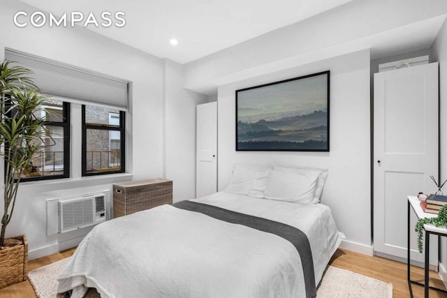 bedroom with recessed lighting, baseboards, a wall mounted air conditioner, and light wood finished floors