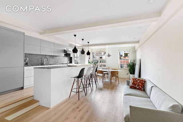 kitchen featuring sink, decorative light fixtures, light hardwood / wood-style flooring, a center island with sink, and backsplash