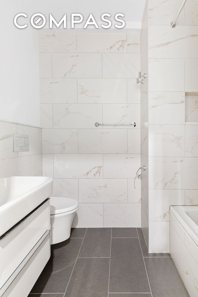 bathroom with tile patterned floors, toilet, a bathing tub, tile walls, and vanity