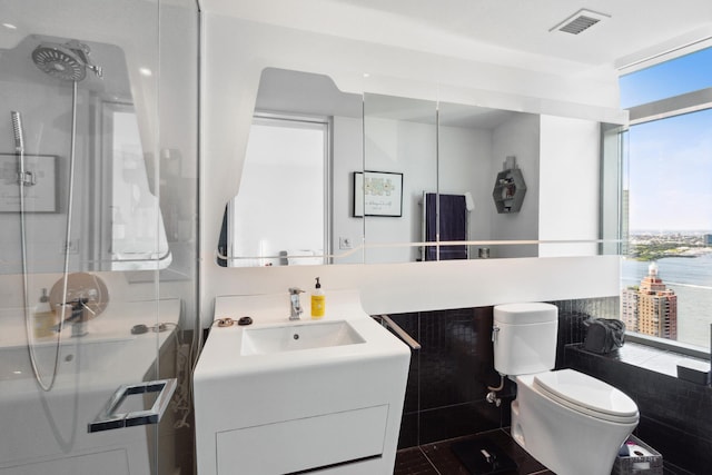 full bath with toilet, a stall shower, visible vents, a wall of windows, and vanity