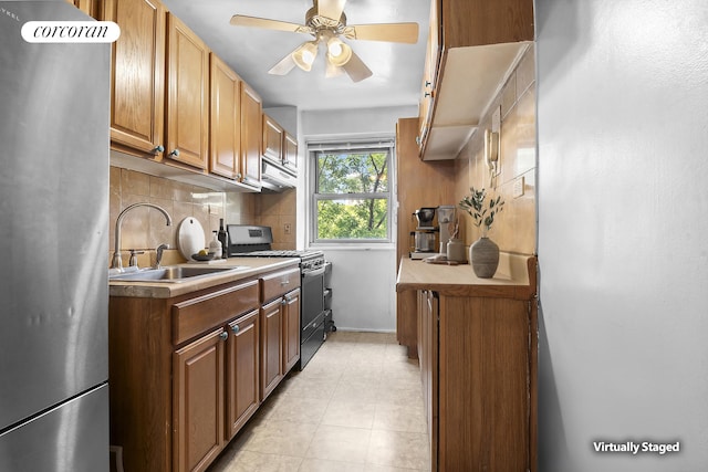 kitchen featuring decorative backsplash, gas range, ceiling fan, freestanding refrigerator, and a sink