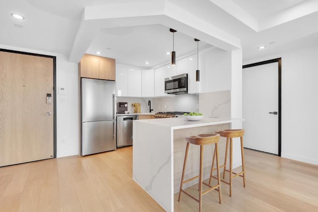 kitchen featuring a breakfast bar, white cabinetry, pendant lighting, stainless steel appliances, and decorative backsplash