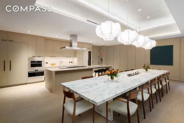 kitchen featuring light wood finished floors, a spacious island, light countertops, a kitchen bar, and wall chimney exhaust hood