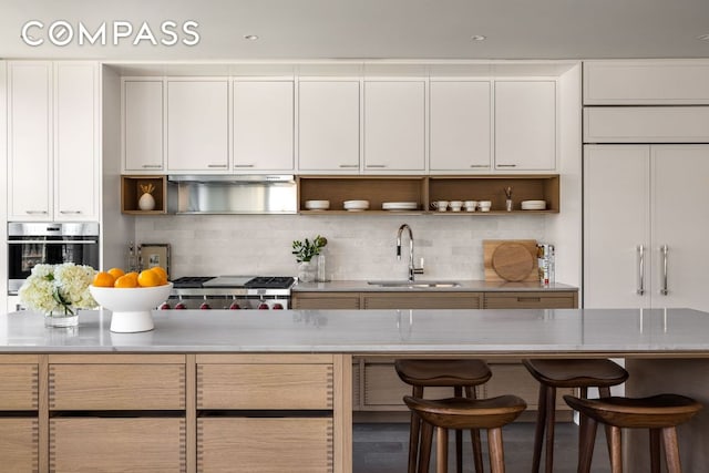 kitchen featuring sink, appliances with stainless steel finishes, white cabinetry, backsplash, and a kitchen breakfast bar