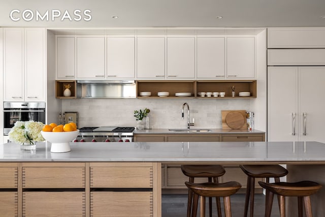 kitchen with a sink, oven, a breakfast bar area, white cabinets, and open shelves