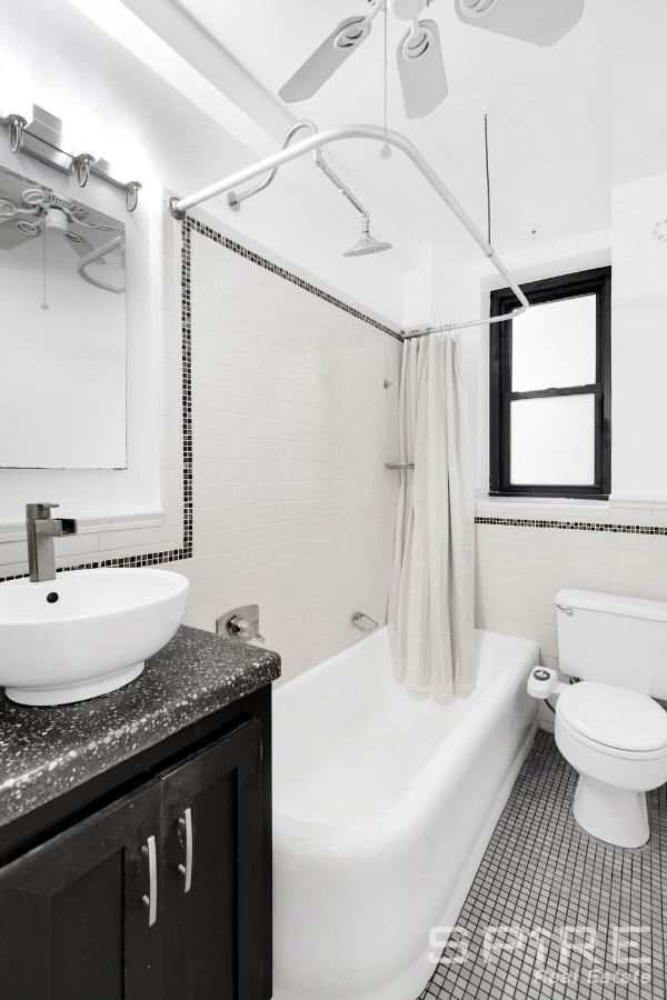 235 E 22nd St Unit 4M, New York City, NY 10010 - full bath featuring shower / bath combo with shower curtain, vanity, toilet, tile patterned flooring, and tile walls