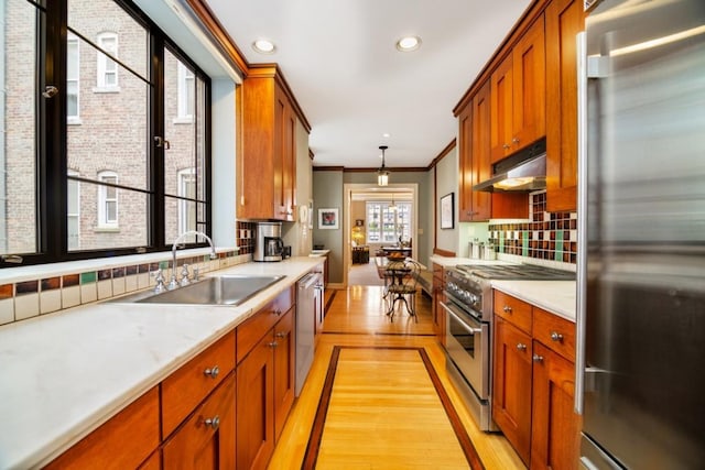 kitchen featuring decorative light fixtures, sink, backsplash, light hardwood / wood-style floors, and stainless steel appliances