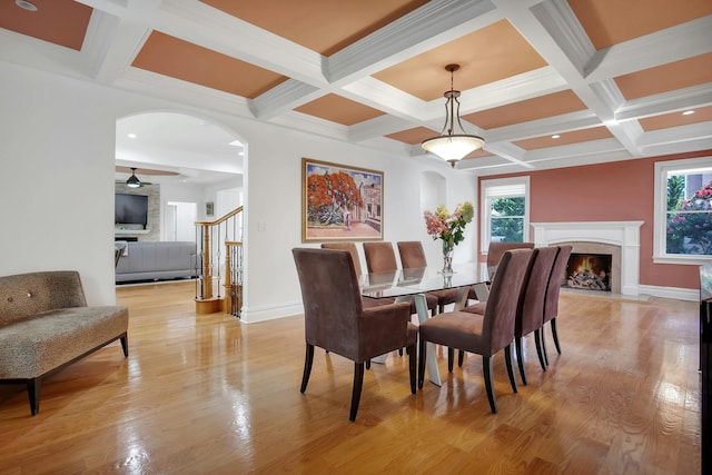 dining space with light wood finished floors, baseboards, stairs, a premium fireplace, and arched walkways