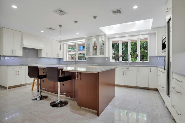 kitchen with premium range hood, visible vents, gas cooktop, a kitchen island, and light tile patterned floors