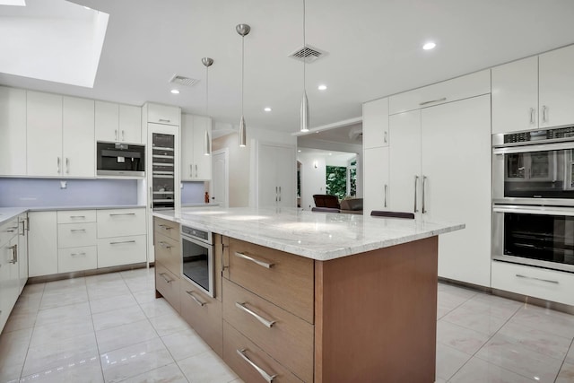 kitchen featuring light stone countertops, visible vents, a skylight, white cabinetry, and double oven