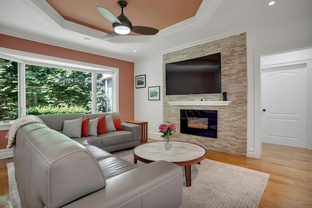 living room featuring a fireplace, a raised ceiling, light wood-style floors, and ornamental molding