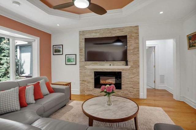 living area with crown molding, a fireplace, a raised ceiling, and wood finished floors