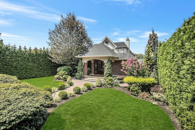 view of front of home featuring brick siding, a chimney, a front yard, and a shingled roof