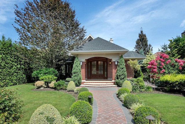 view of front of property with a front lawn, french doors, roof with shingles, brick siding, and a chimney