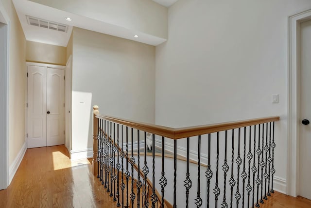 hall with wood finished floors, an upstairs landing, visible vents, and baseboards